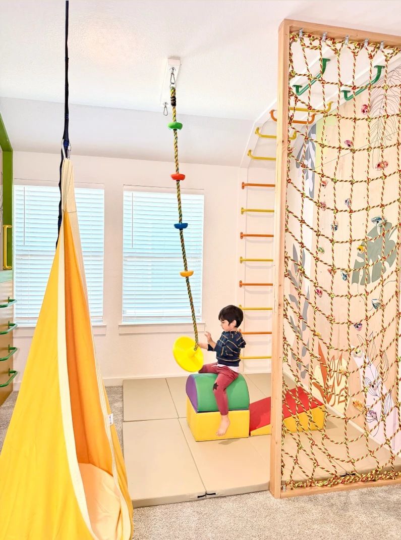 A playroom with a pod swing, a rope swing and a cargo-net climbing frame