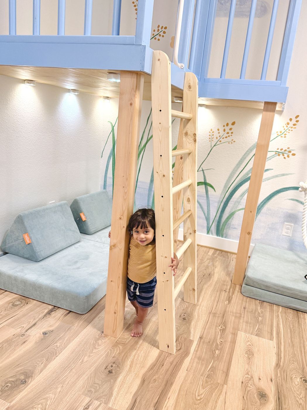 Child beside wooden play loft ladder