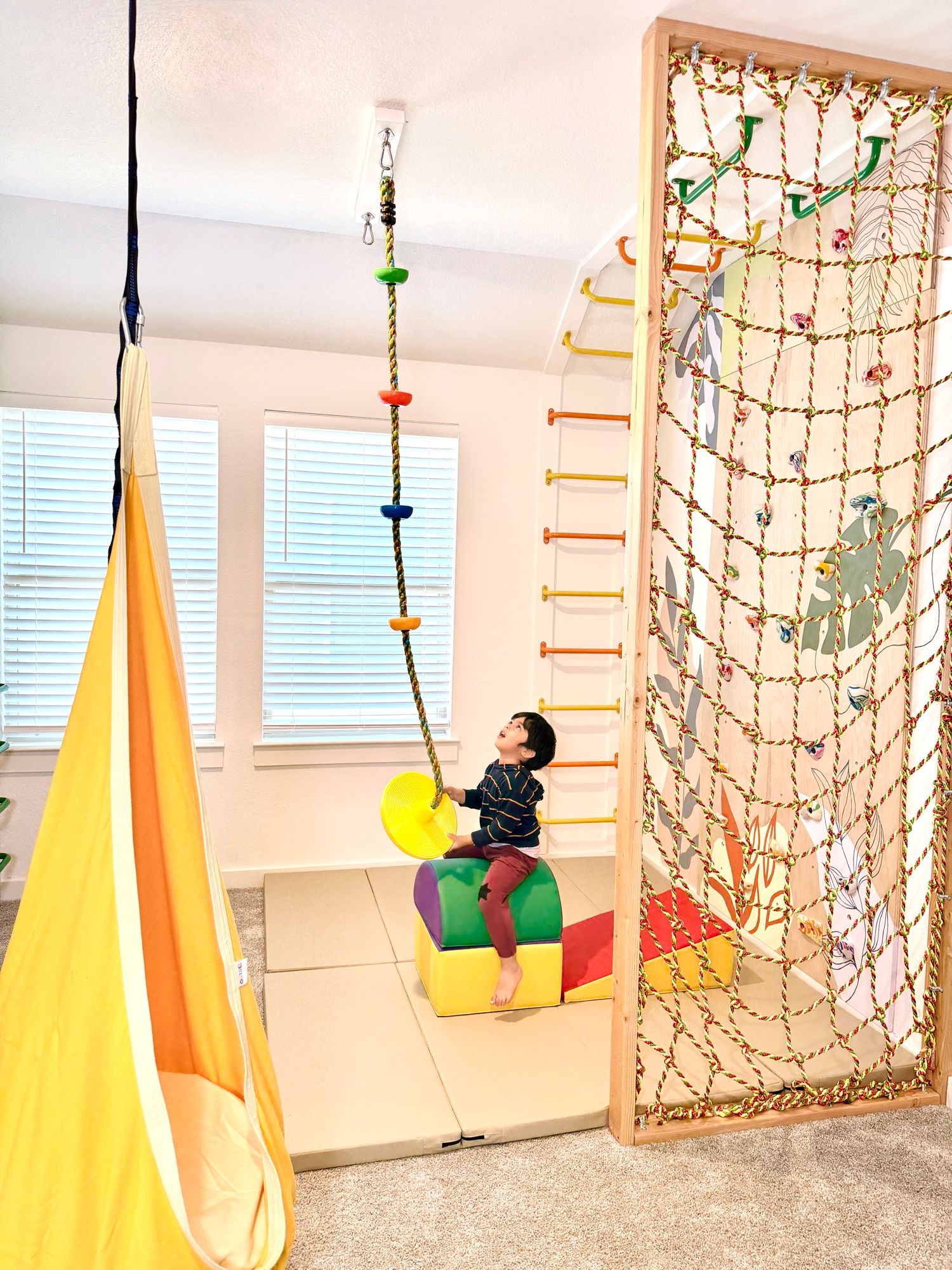 A child on the disc swing beside the rope net and the yellow pod swing