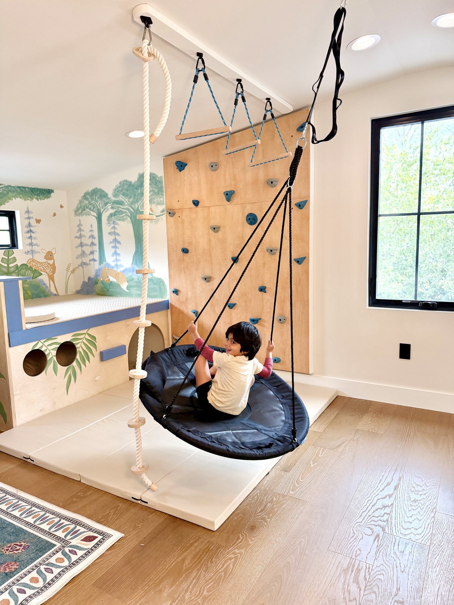 A child on the round nest swing beside the climbing wall