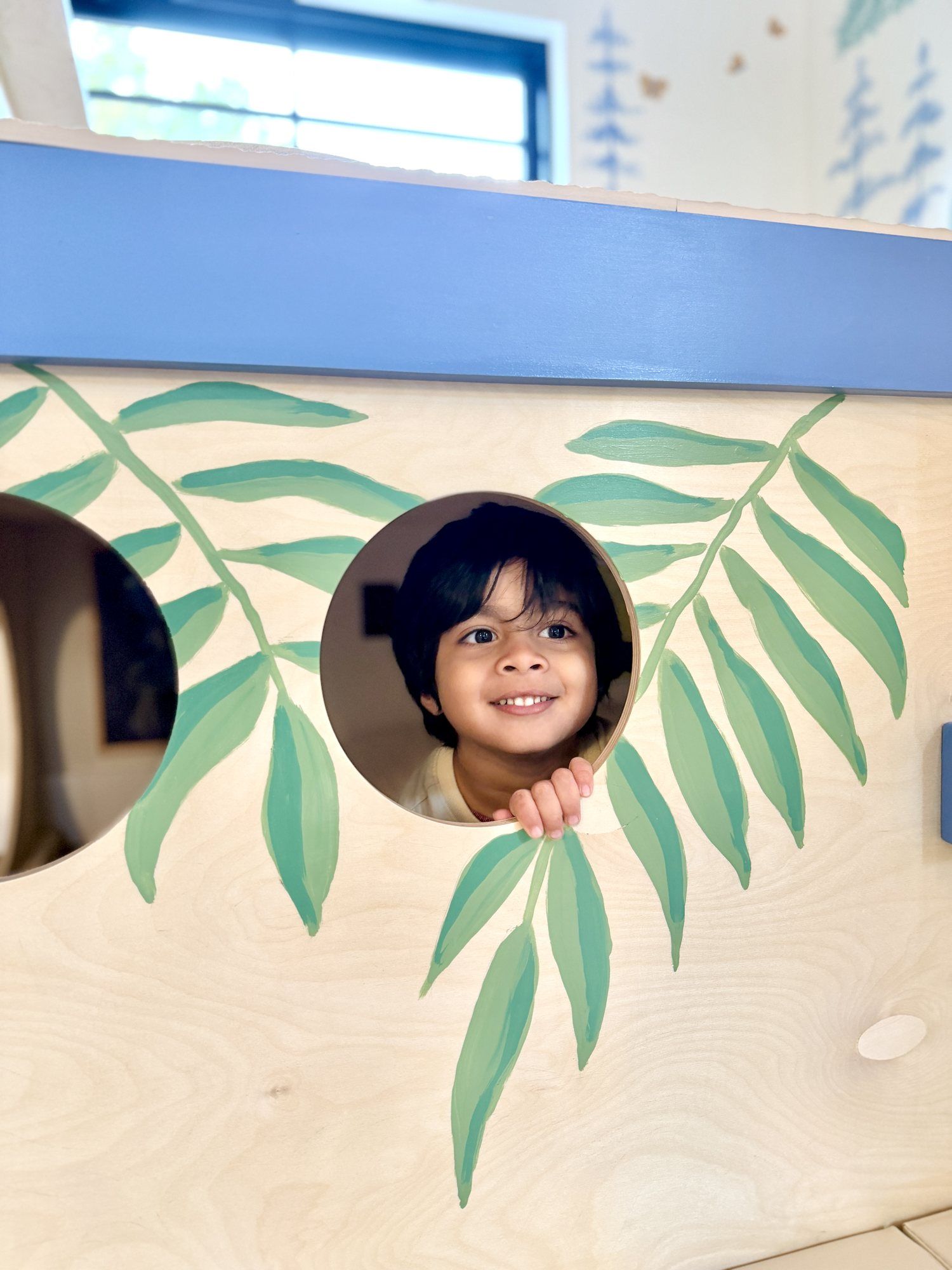 A child peeking through a leaf-painted round window