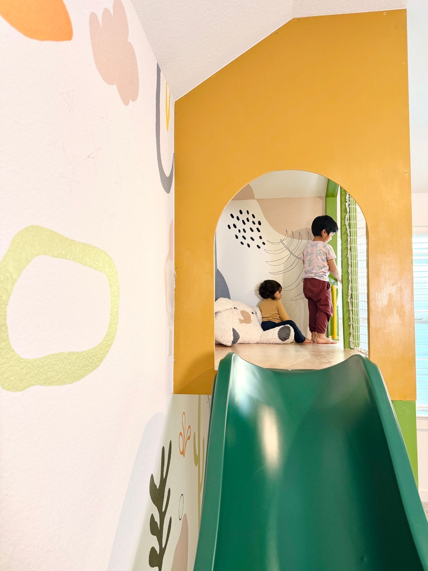 Two children inside the yellow playhouse, at the top of the slide