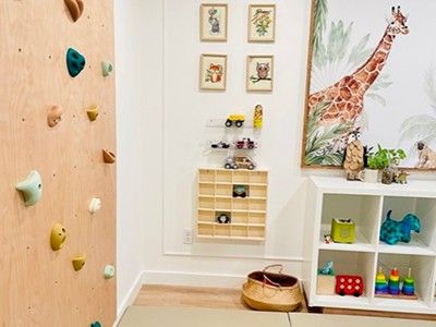 A finished playroom with a birch climbing wall, giraffe mural and toy shelves