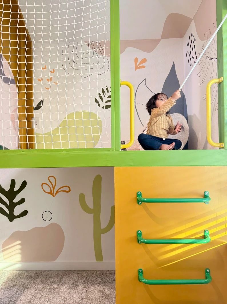 A child in a netted playhouse loft above a ladder of green rungs