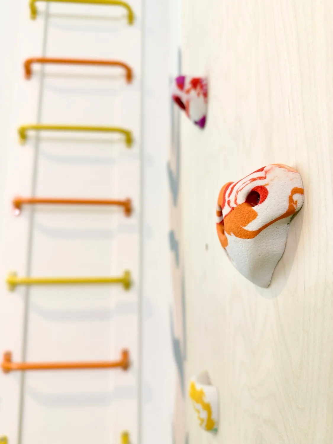 Close-up of a marbled climbing hold on a plywood wall, with colourful monkey bars beyond