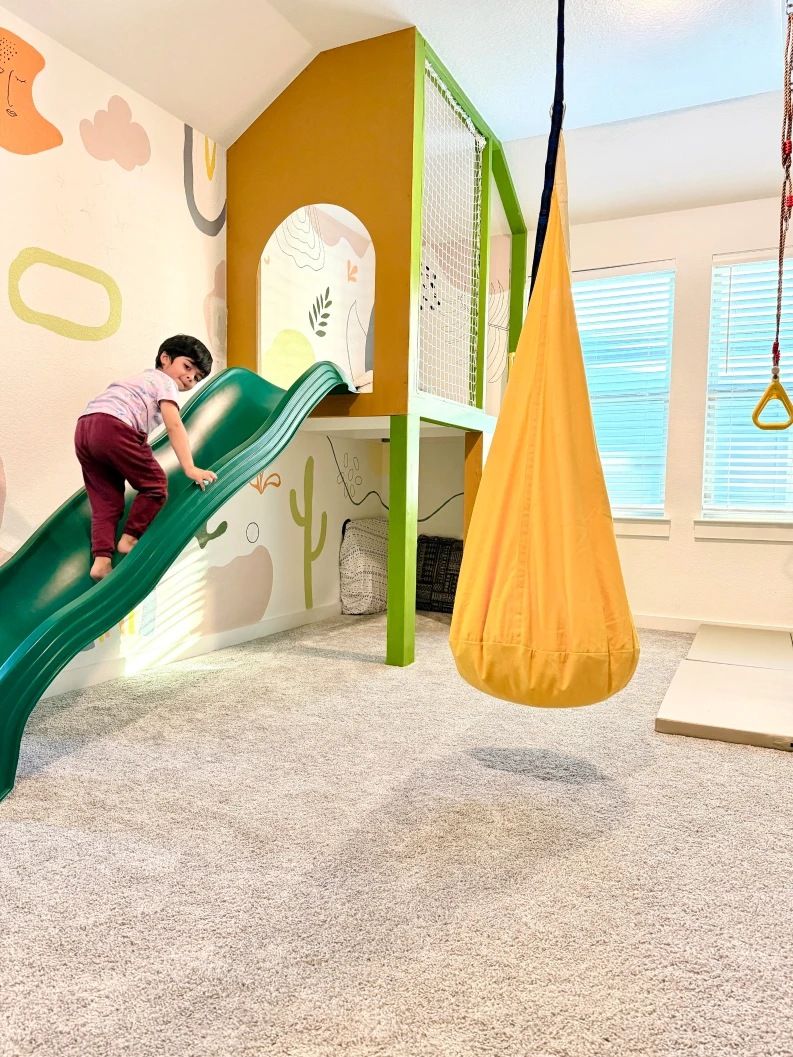 A child climbing a green slide up to an arched hideaway