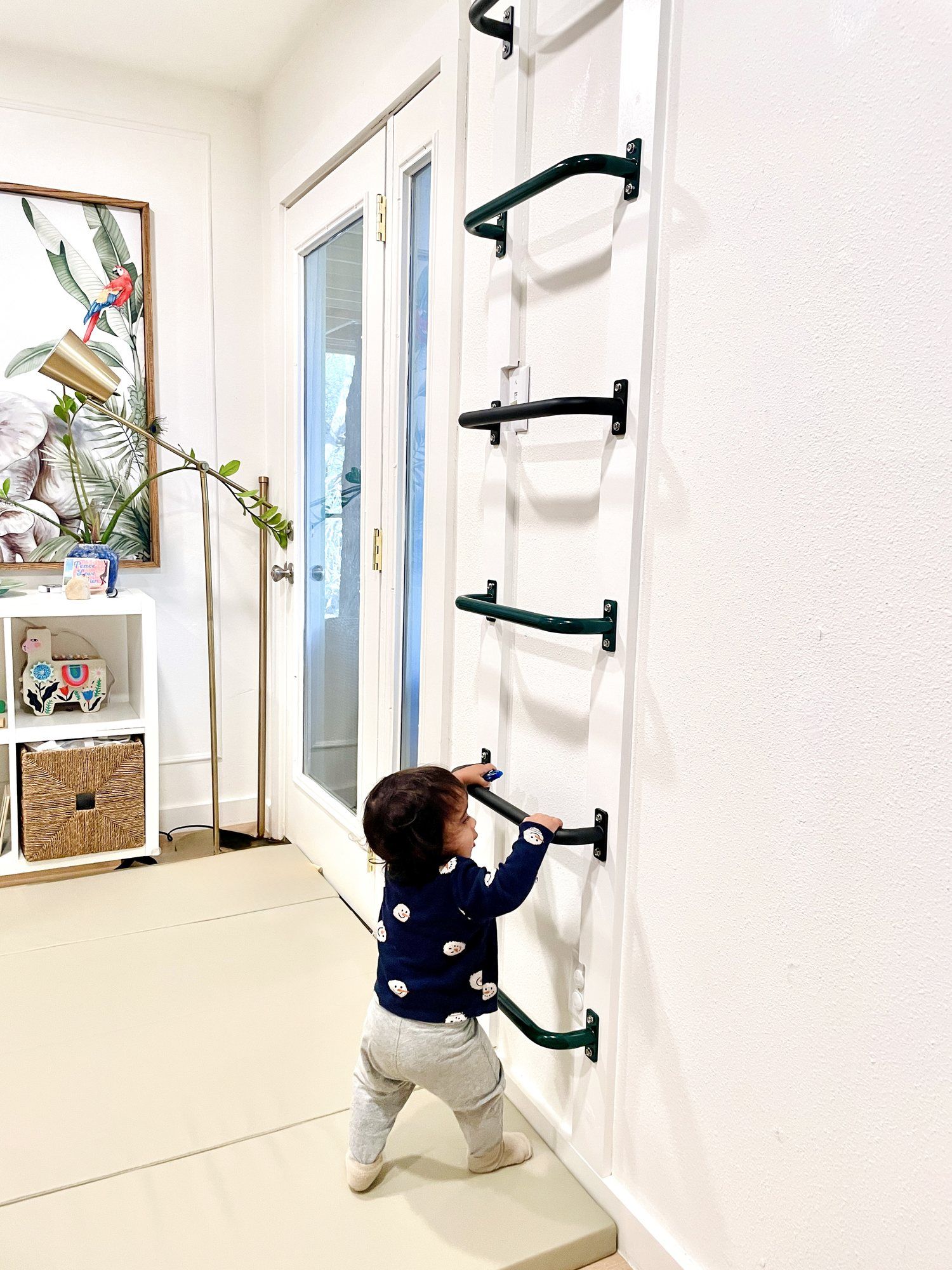 A toddler climbing the black wall bars